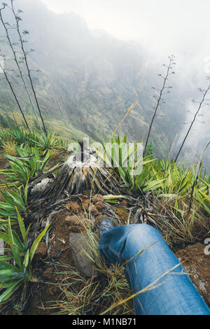 Leg de voyageur séjournant sur la corniche au-dessus de la verte vallée brumeuse recouvert d'agaves dans l'île de Santo Antao Cabo Verde Banque D'Images