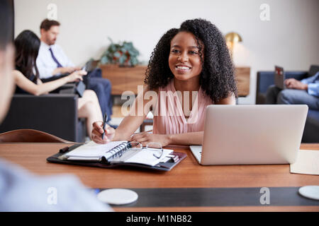 Jeune femme noire à un bureau à la recherche d'un collègue d'en face Banque D'Images