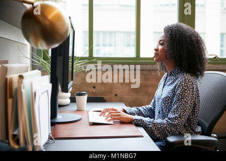 Femme noire le travail à l'ordinateur dans un bureau, vue latérale Banque D'Images