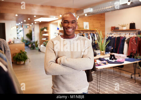 Jeune homme noir souriant pour appareil photo dans un magasin de vêtements Banque D'Images