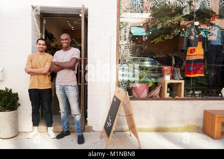 Deux jeunes hommes smiling to camera à l'extérieur de leur magasin de vêtements Banque D'Images