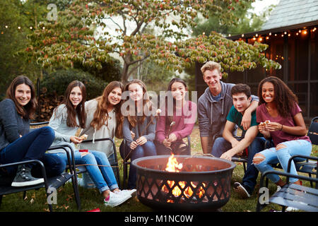 Adolescents assis autour d'un foyer à l'appareil photo en souriant Banque D'Images