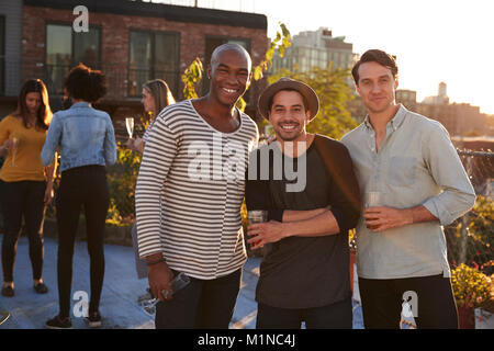 Trois amis de sexe masculin à un toit-party smiling to camera Banque D'Images