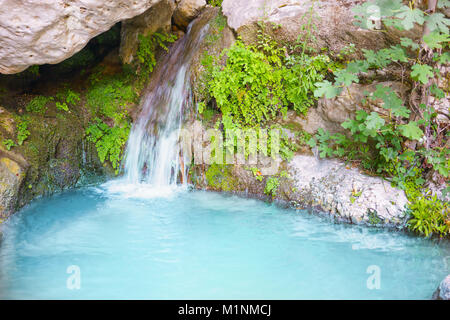 Chute dans un printemps vert forêt entourée par des pierres, eau turquoise sur un paysage naturel impressionnant Banque D'Images