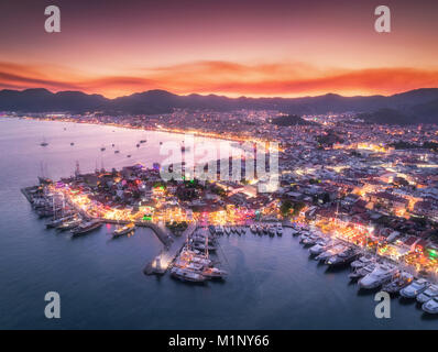 Vue aérienne de bateaux et belle ville la nuit en Marmaris, Turquie. Un paysage extraordinaire avec des bateaux à Marina Bay, la mer, les lumières de la ville, montagnes, ciel rouge Banque D'Images
