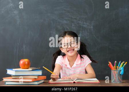 Happy happy female student faire leurs devoirs en classe sur l'arrière-plan et tableau à la caméra à l'école. retour au concept. Banque D'Images