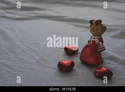 Cute Bear avec des coeurs autour d'elle s'affiche au-dessus d'un drap de lit blanc. Laissant l'espace à gauche pour le texte et les messages. Banque D'Images