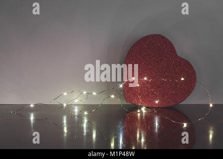 Big red box coeur sur le dessus d'une table en bois avec un fond blanc avec des lumières. Laissant l'espace à gauche pour le texte et les messages. Banque D'Images