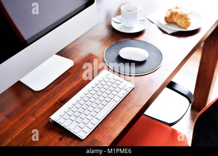 Scène de travail avec petit-déjeuner. Petit-déjeuner de base sur un lieu de travail, un croissant et une tasse à café. Ordinateur, collation et boisson chaude, de scène, pause. Banque D'Images