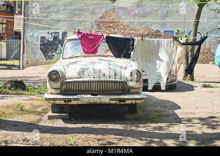 Old vintage voiture pour pièces dans un style soviétique cour où le linge est séché sur une corde Banque D'Images