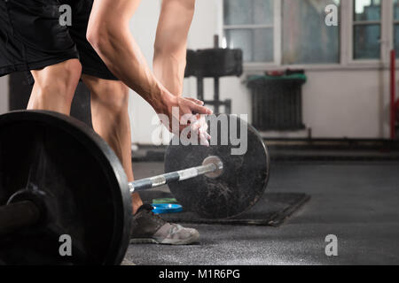 L'haltérophile part l'application de talc avant de faire de l'exercice d'haltères avec In Gym Banque D'Images