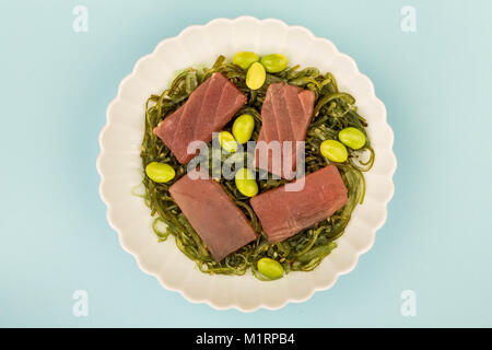 De style japonais, sashimi de thon cru sur un lit d'algues marinées avec Edamame Beans sur un fond bleu Banque D'Images