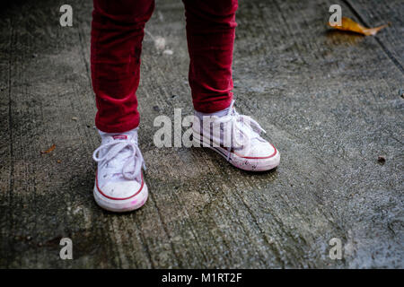 Les jambes des filles en pantalon rouge, avec des chaussures humide et sale avec de la peinture sur un jour de pluie Banque D'Images