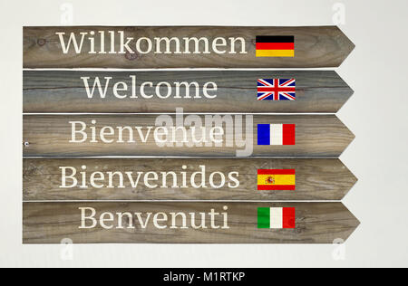 Pancarte en bois montrant bienvenue dans cinq langues différentes avec leurs drapeaux et indications sur fond gris clair Banque D'Images