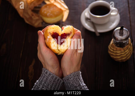 Man hands holding heart-shaped donut avec berry jam Banque D'Images