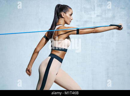 Femme forte, à l'aide de bande de résistance dans sa routine d'exercice. Photo du modèle de remise en forme d'entraînement sur fond gris. Force et motivation Banque D'Images