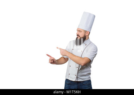Charmant jeune homme chef cuisinier pointer du doigt en uniforme blanc sur fond blanc Banque D'Images