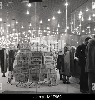 Années 1950, historique, du temps le soir et les acheteurs parisiens toutes les marchandises dans un magasin de détail fastueux avec une grande entrée en verre près de l'Avenue des Champs-Elysées, avec un grand écran ou un rack de quotidiens français situés à l'avant, Paris, France. Banque D'Images