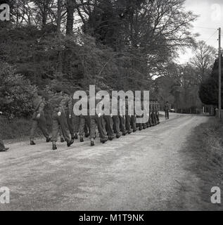 1955, historiques, Bucks, en Angleterre, d'une troupe de soldats britanniques sur un exercice de formation à l'extérieur, les soldats marchent sur une piste de gravier à travers une zone boisée. Banque D'Images