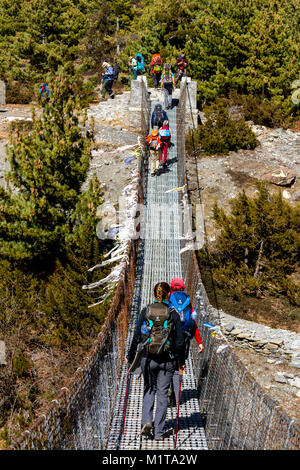 Touristes traversant un pont suspendu sur l'Annapurna, Trek Himalaya. Le circuit de l'Annapurna est un trek dans les montagnes de l'Annapurna Népal central Banque D'Images