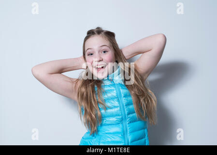 Smiling girl in gilet bleu avec les mains derrière la tête sur fond blanc Banque D'Images