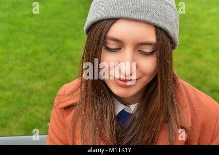 Jeune femme européenne à l'extérieur, dans un chapeau gris. Regarder vers le bas. Souriant doucement. Portrait. Photo horizontale Banque D'Images