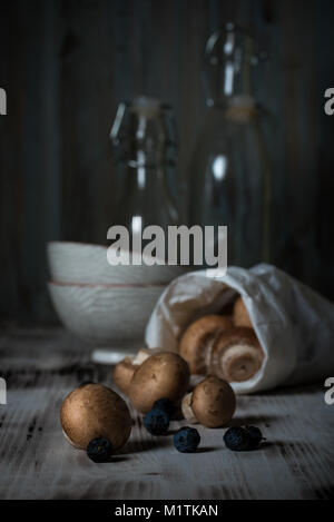 Photo verticale avec brun déversé des champignons comestibles à partir de sac de papier. Les champignons sont sur vintage planche en bois avec deux bols et deux bo de verre Banque D'Images