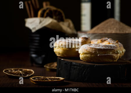 Photo horizontale avec trois des bouffées par crème de lait, de vin et de bâtonnets de cannelle. Les inhalations sont couverts par du sucre en poudre. Peu de r d'orange séchée Banque D'Images