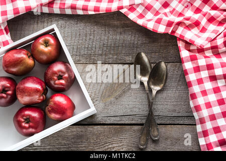 Pommes rouges bien mûrs en bouleau-box sur planche de bois avec une serviette autour de rouge à carreaux, et les cuillères et copie de l'espace pour votre recette. Banque D'Images