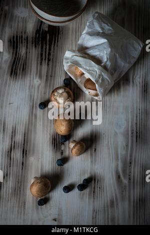 Photo verticale avec vue de dessus sur le brown des champignons comestibles à partir de sac de papier. Les champignons sont sur vintage bois blanc avec couleur et usés Banque D'Images