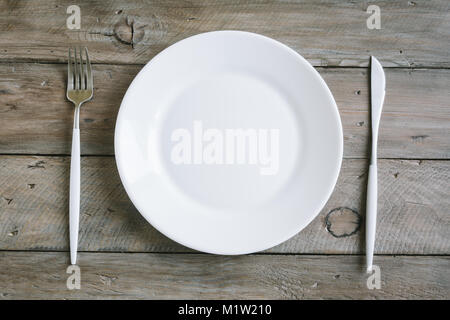 Table avec plaque blanche et moderne, des couverts (fourchette et couteau) sur fond de bois, vue du dessus, copiez l'espace. Banque D'Images