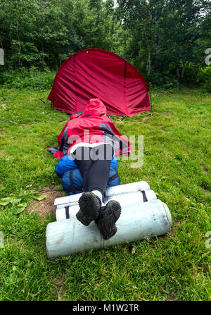 Girl couché dans l'herbe près de la tente dans les bois Banque D'Images