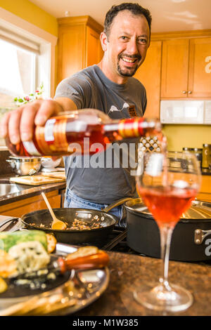 Un homme de verser le vin dans un verre dans une cuisine qu'il cuisine. Banque D'Images