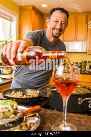 Un homme de verser le vin dans un verre dans une cuisine qu'il cuisine. Banque D'Images