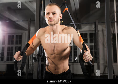 Low Angle View of a Young Man Exercising With Athlète Suspension Trainer In Gym Banque D'Images
