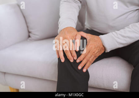 Hauts homme assis sur un canapé dans la salle de séjour à la maison et toucher son genou par la douleur Banque D'Images