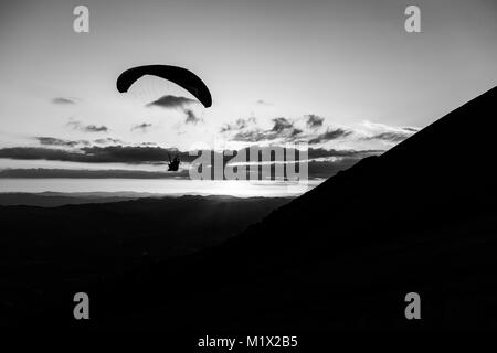 Beau coup d'une silhouette parapente voler au-dessus de Monte Cucco (Ombrie, Italie) avec le coucher du soleil sur l'arrière-plan Banque D'Images