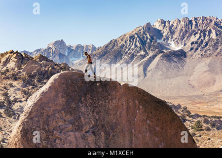 L'homme grimpe sur rocher de granit énorme rocher dans la région de babeurre de Bishop, en Californie avec la Sierra Nevada derrière Banque D'Images