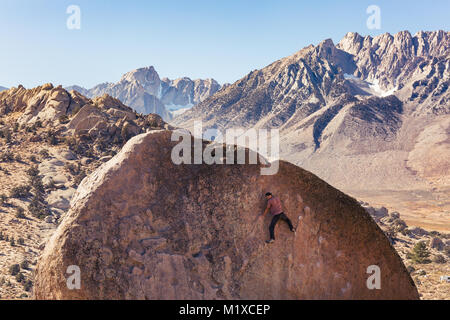 L'homme grimpe sur rocher de granit énorme rocher dans la région de babeurre de Bishop, en Californie avec la Sierra Nevada derrière Banque D'Images