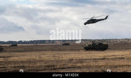 Des soldats américains de Kronos Troop, 3e Escadron, 2e régiment de cavalerie, conduire leur Strykers à leurs positions de combat tandis qu'un hélicoptère MI-24 fournit un appui aérien puisqu'ils participent à un exercice de tir réel de l'OTAN coordonné par le 1er Bataillon polonais 15e Brigade mécanisée à une gamme près de la zone d'entraînement Bemowo Piskie, Pologne, le 30 janvier 2018. La multinationale, unique, composé d'Américains, Britanniques, croate et soldats roumains servir avec la 15e Brigade mécanisée polonaise comme une force de dissuasion dans le nord-est de la Pologne à l'appui de l'OTAN vers l'amélioration de la présence. (U.S. Army Banque D'Images