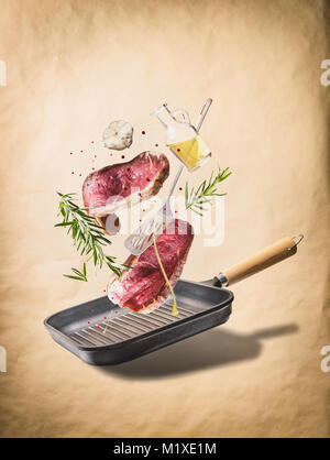 La viande de boeuf cru voler des steaks, de fines herbes, d'huile et des épices avec poêle et des ustensiles de cuisine, au fond beige naturel, vue de face. Flying food co... Banque D'Images