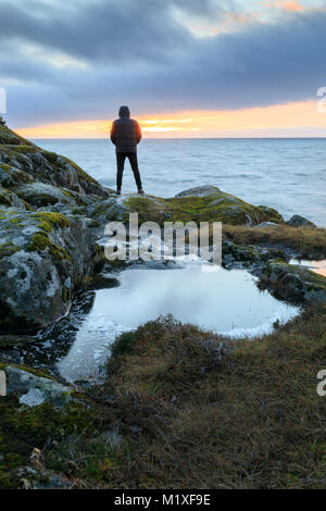 L'homme sur la côte rocheuse pendant le coucher du soleil à Stora Lund, Suède