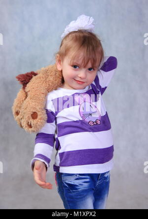 Sur un fond gris est une petite fille avec un chien dans ses mains. Elle est vêtue d'une veste et un jean. Banque D'Images