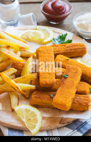 Bâtonnets de poisson frit avec des frites. Les bâtonnets de poisson sur fond de bois. Les bâtonnets de poisson avec pommes de terre frites et de citron prêt à manger. Banque D'Images