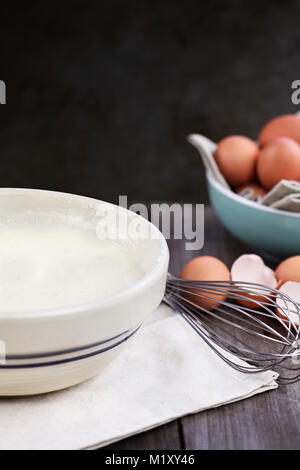 Bol de mélange de la pâte à crêpes faites maison avec des oeufs frais de la ferme brown en arrière-plan. L'extrême profondeur de champ. Parfait pour Mardi Gras. Banque D'Images