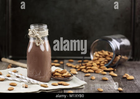 Chocolat bio le lait d'amande dans une bouteille en verre avec amandes renversé sur une table en bois rustique. Banque D'Images