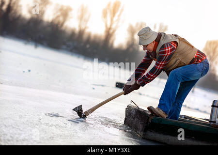 Vieux Pêcheur percer un trou pour l'hiver la pêche sur le lac gelé Banque D'Images