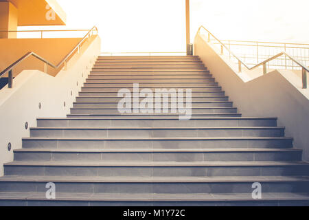 Vue avant du vide escalier en béton avec rampe en métal qui vont jusqu'en dernier étage avec la lumière du soleil dans l'arrière-plan. Banque D'Images