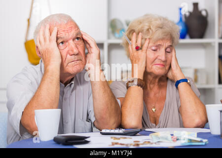 Couple frustrés face à des ennuis financiers table avec titres, espèces et calculatrice Banque D'Images