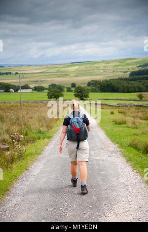 Femme marche sur route de campagne déserte en Cumbria, Angleterre, Royaume-Uni. Banque D'Images